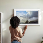 Bilder aufhängen - Beitragsbild: Frau hängt Bild mit Rahmen an die Wand